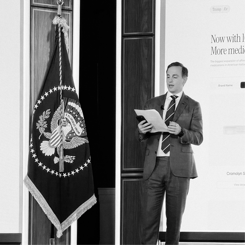 Presenter beside the presidential seal flag with a TrumpRX slide on screen