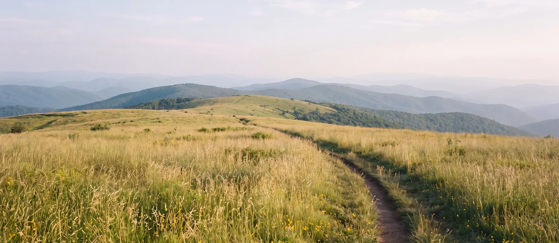 A footpath through open grassland, with layered ridgelines receding into haze beyond