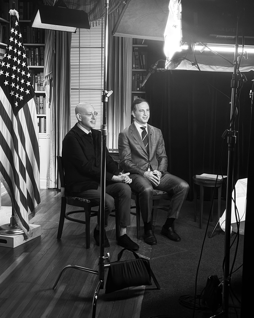Two guests seated for an on-camera interview with an American flag behind them